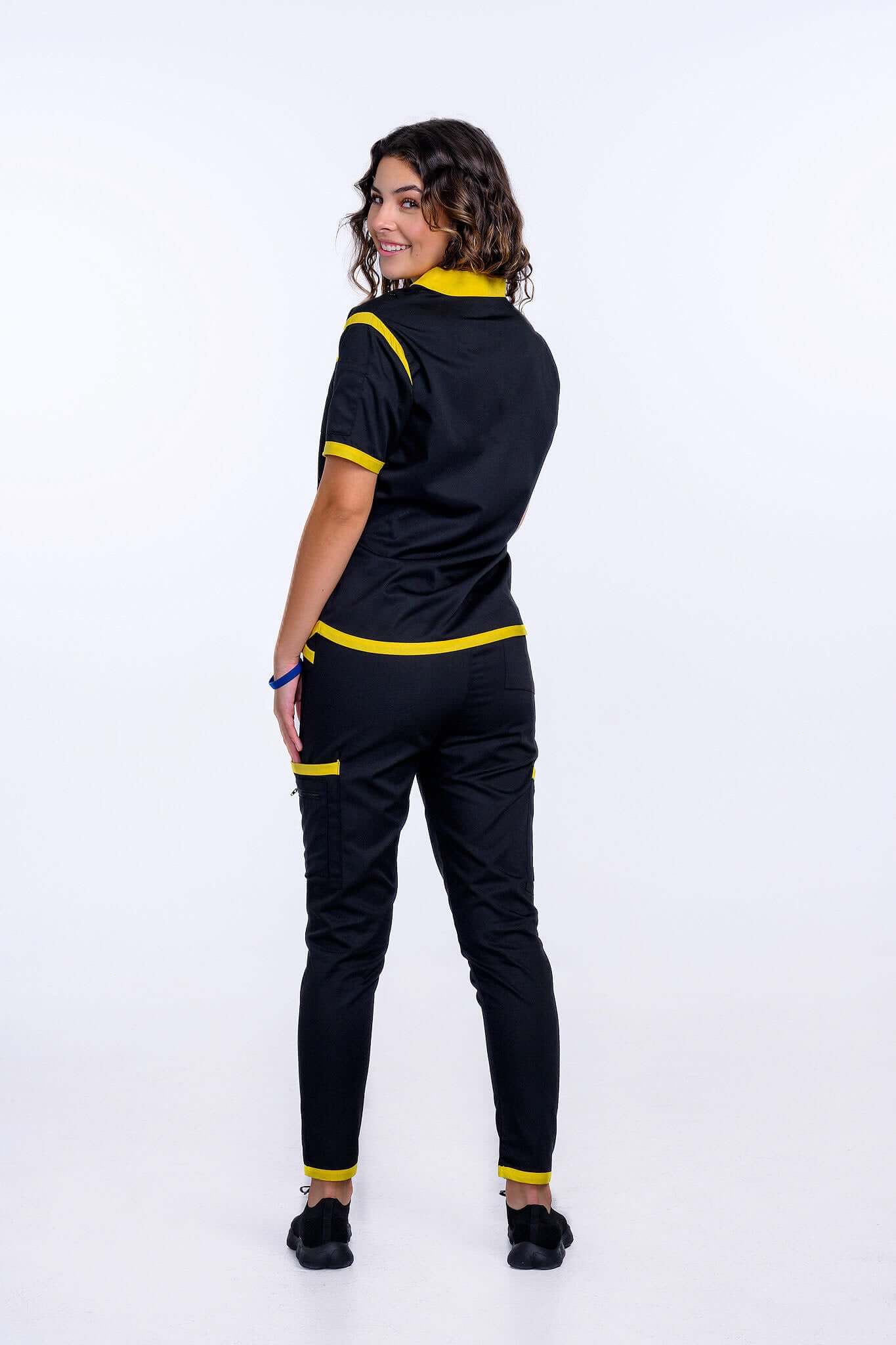 Woman wearing TangoScrubs Women's Jet Black and Yellow Scrub Pants with matching top, showcasing back view style and comfort.